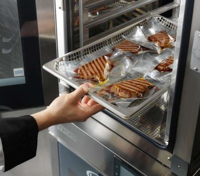 Hand removing a tray of meat packaged in MULTI.Day bags from the Unox hot holding system.