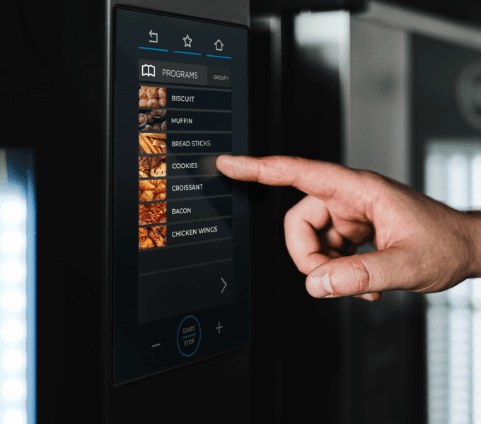Hand selecting a cooking programme on the digital control panel of a Unox professional combi oven.