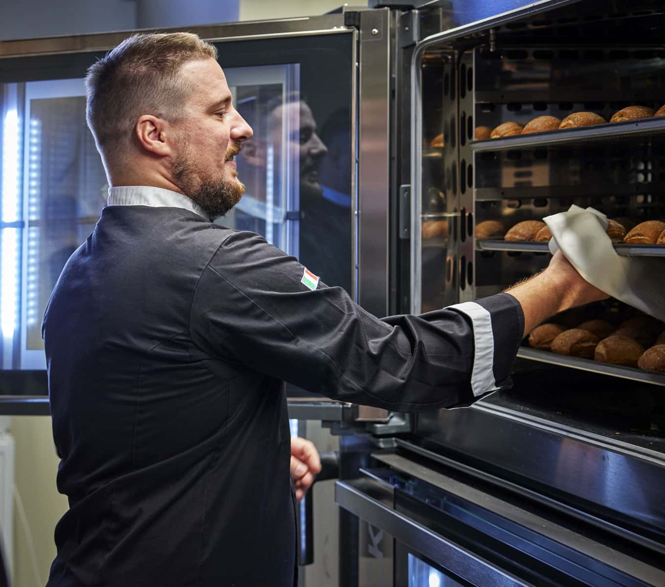 Male chef taking a tray of croissants out of a Unox combi oven for professional pastry