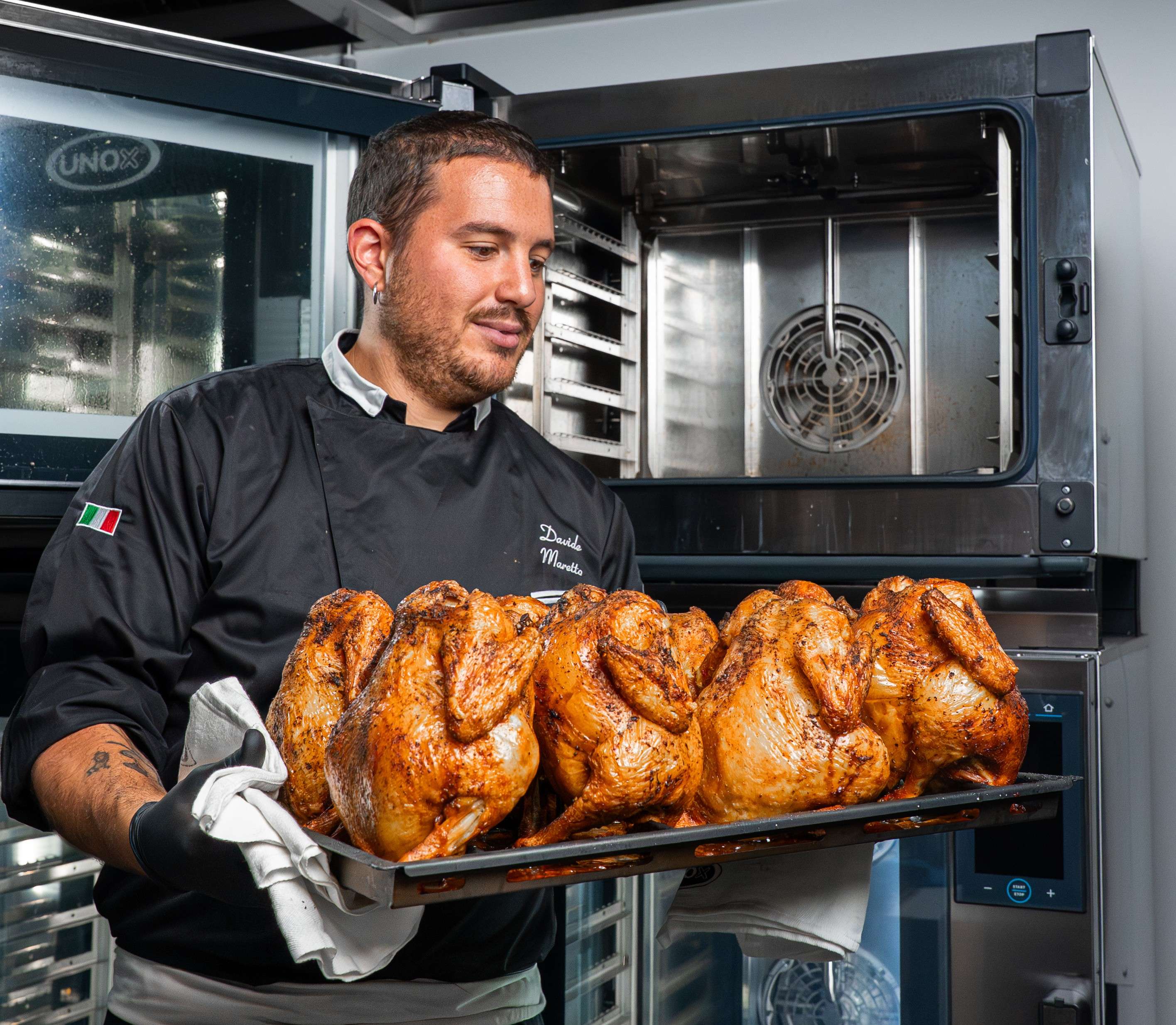 chef uomo guarda la teglia di polli estratta dal forno combinato professionale Unox alle sue spalle
