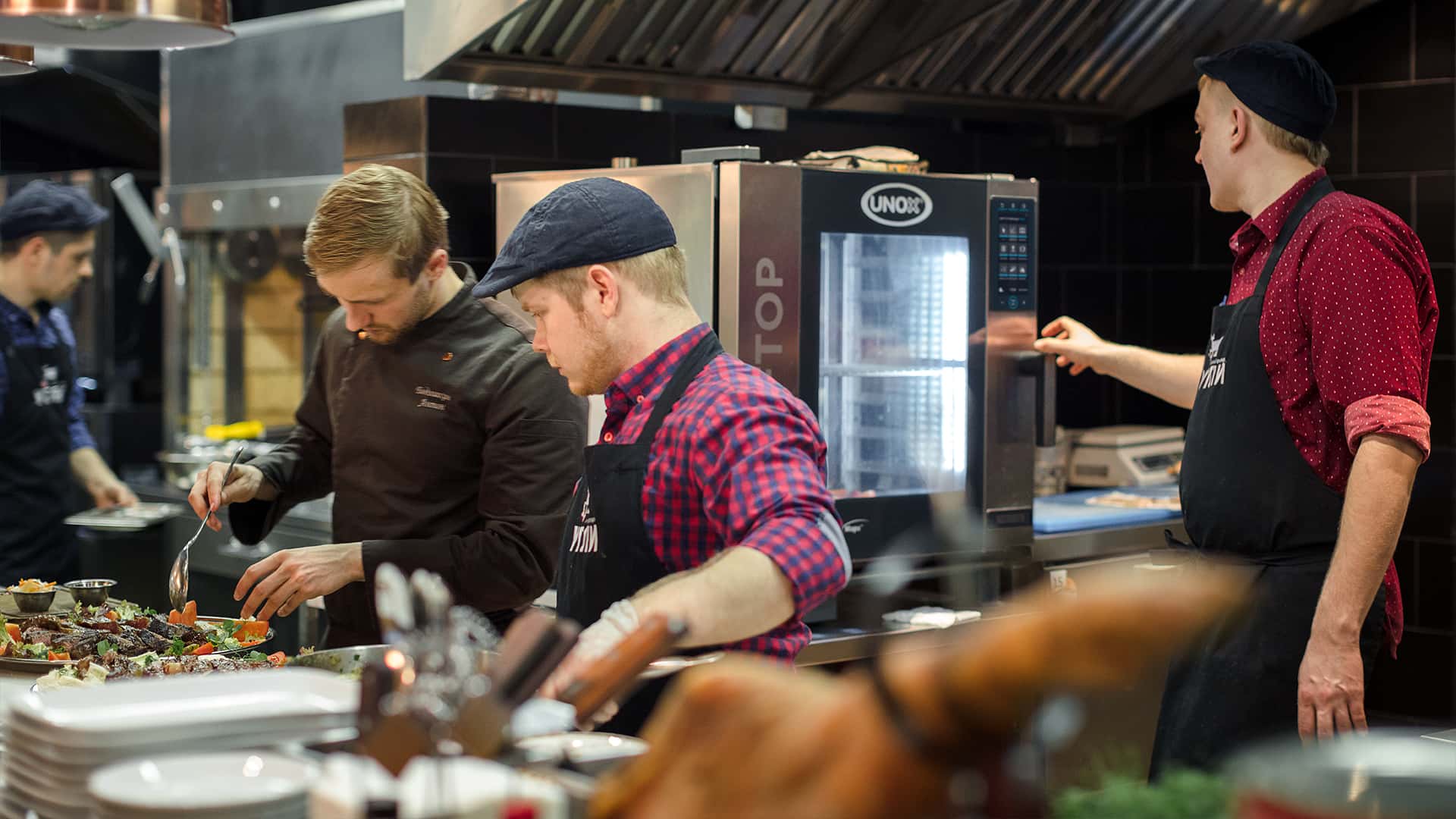 Team di chef uomini al lavoro in cucina, con forno professionale combinato Unox sullo sfondo.