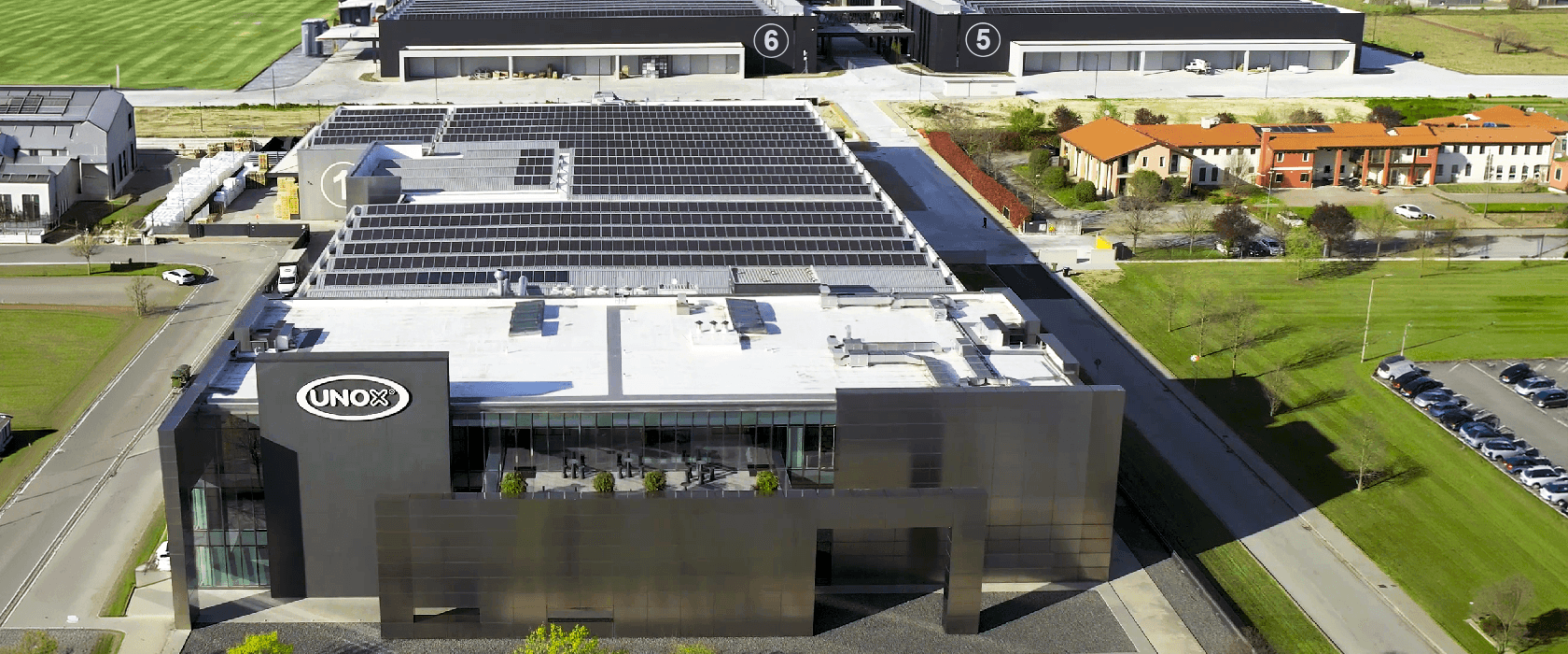 Foto aérea de un campo de paneles solares entre un bloque de edificios y rodeado de campos verdes.