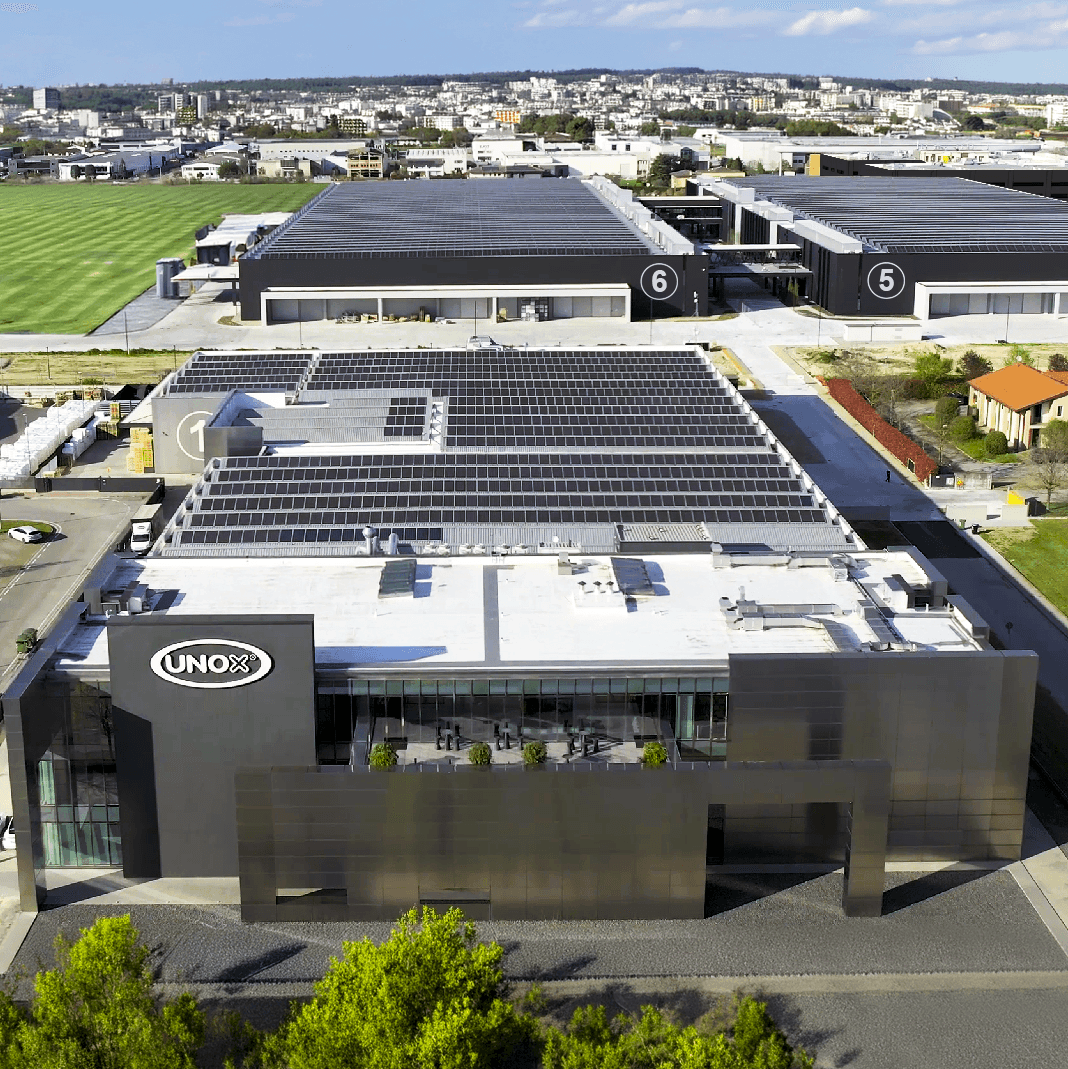 Foto aérea de un campo de paneles solares entre un bloque de edificios y rodeado de campos verdes.