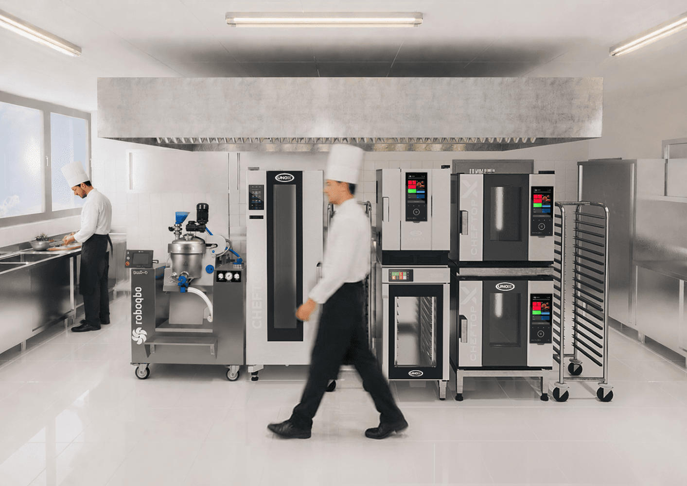 Chef walking past Unox commercial combi ovens and a Qbo multifunction robot, while another operator works at a counter in a professional kitchen