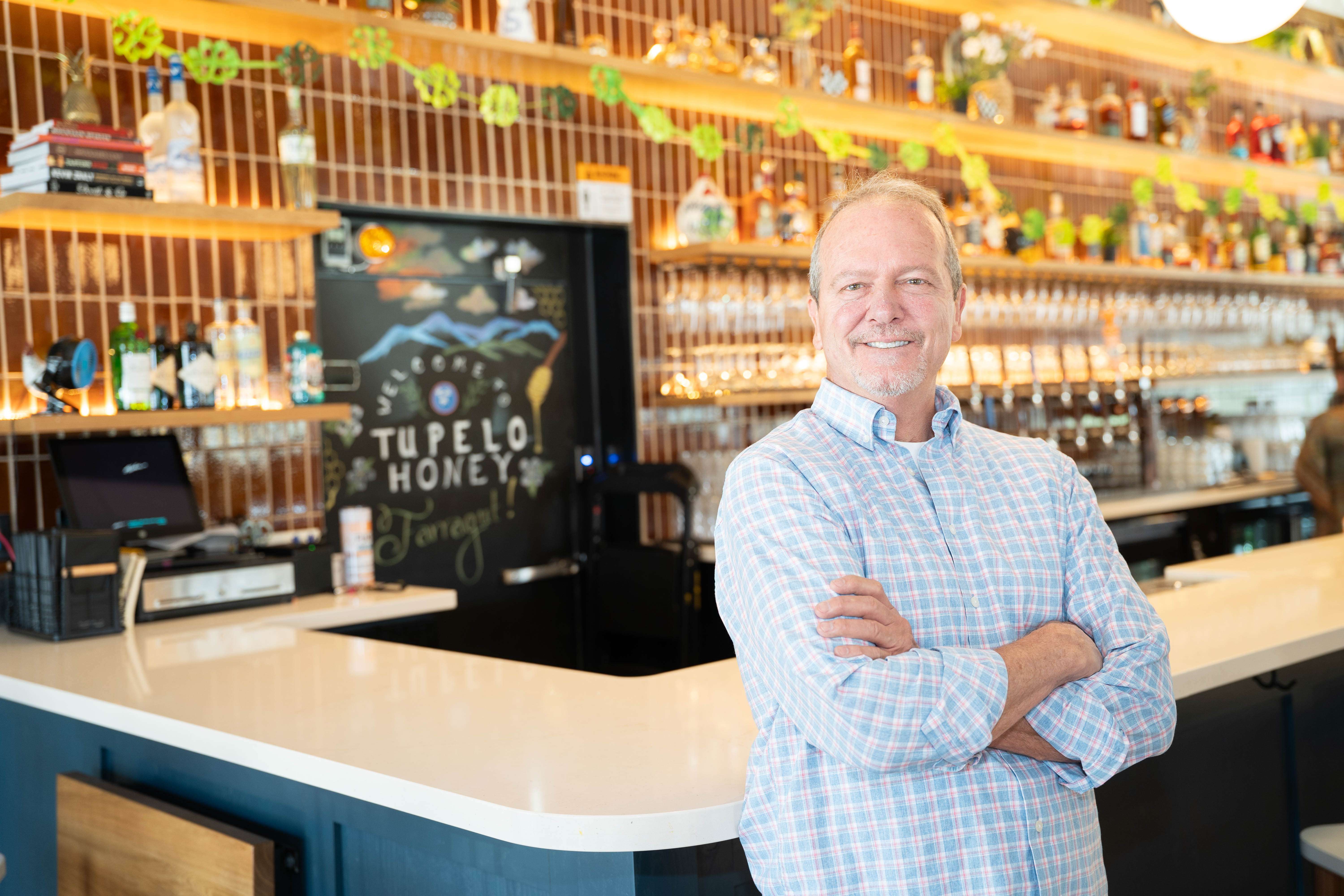 Restaurant manager stands with his arms crossed in front of the bar counter at Tupelo Honey.