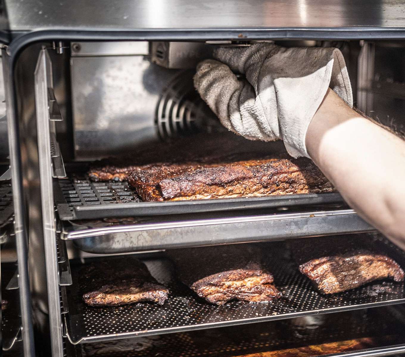 Une chambre de cuisson ouverte d'un four combiné professionnel Unox avec des côtes de porc à l'intérieur et un accessoire de fumage installé